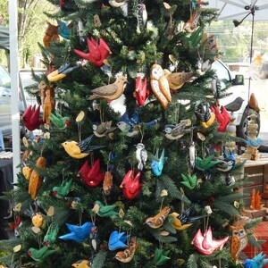 May include: A Christmas tree decorated with hand-painted wooden ornaments. The ornaments feature a variety of birds, owls, and other woodland creatures. The ornaments are painted in bright colors, including red, blue, green, yellow, and brown.