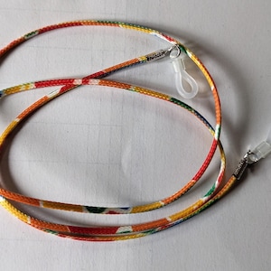 May include: A colourful patterned eyeglass chain with two clear plastic clasps. The chain is made of a woven fabric with red, yellow, green, and blue stripes.