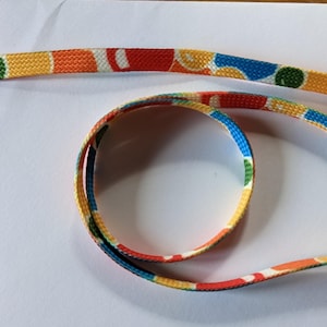 Peut inclure: Un cordon coloré à motifs avec deux clips en plastique à chaque extrémité. Le cordon est fait d'un tissu tissé avec un motif jaune, orange, rouge, bleu et vert.