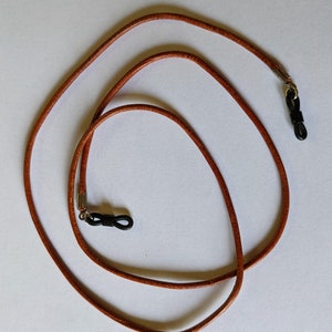 May include: A brown leather eyeglass chain with two black metal and plastic clasps.