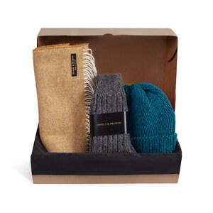 May include: A gift box filled with winter accessories. The box contains a mustard yellow herringbone scarf, a pair of grey knitted socks, and a teal blue knitted beanie. The box is lined with black fabric and has a label that reads "Orwell & Browne".