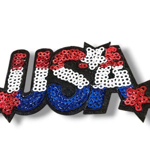 May include: A red, white, and blue sequined patch with the word "USA" and two stars. The patch is made of felt and has a black backing.