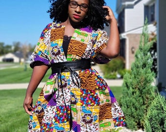 May include: A colorful patchwork kimono-style top with a black leather belt. The top features a variety of patterns, including animal print, geometric shapes, and floral designs. The sleeves are short, and the garment is worn over a black top and leggings.