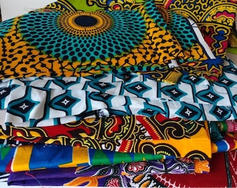 May include: A stack of colorful fabric scraps with various patterns, including geometric, floral, and abstract designs. The fabrics are in shades of blue, green, yellow, red, and white.