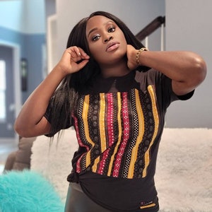 May include: A black t-shirt with a colorful geometric pattern. The pattern features stripes of yellow, red, and black with intricate designs.