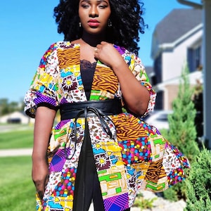 May include: A vibrant patchwork kimono jacket, cinched at the waist with a black belt. The jacket displays a variety of patterns, including animal prints and geometric shapes. The model is wearing a black top and leggings.