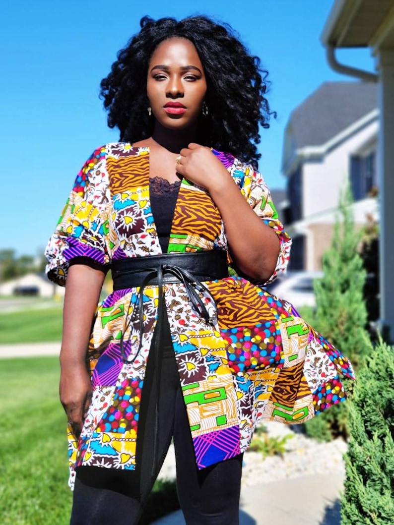 May include: A vibrant patchwork kimono jacket, cinched at the waist with a black belt. The jacket displays a variety of patterns, including animal prints and geometric shapes. The model is wearing a black top and leggings.