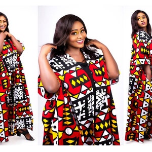 May include: A woman is wearing a long, red, yellow, black, and white patterned dress with a geometric design. The dress has a V-neck and short sleeves.