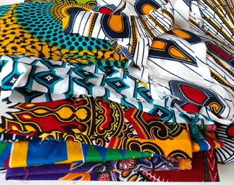 May include: A stack of colorful fabric with various patterns, including geometric shapes, floral designs, and abstract patterns. The fabric is a mix of white, blue, red, yellow, and black.
