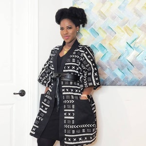 May include: A black and white patterned kimono with a black belt and black leggings. The kimono has a geometric pattern with white accents. The person is wearing a gold necklace.