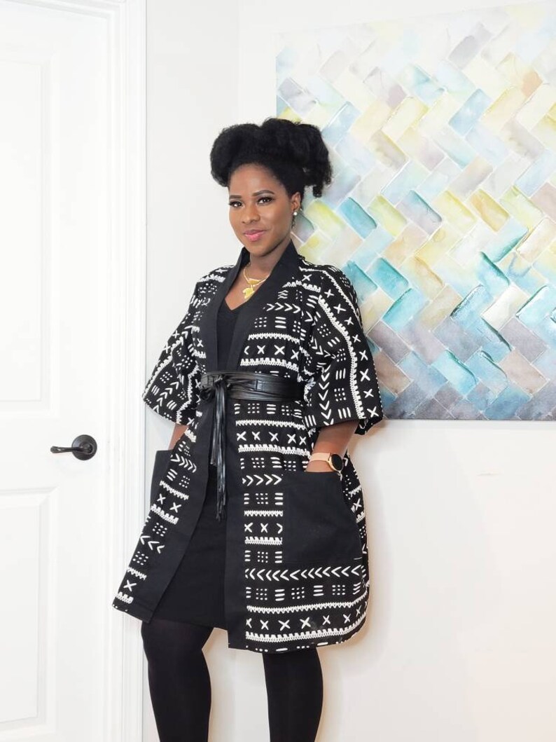May include: A black and white patterned kimono with a black belt and black leggings. The kimono has a geometric pattern with white accents. The person is wearing a gold necklace.