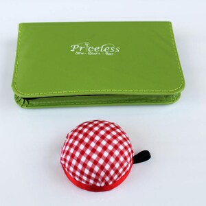 May include: A green sewing kit with the text "Priceless Sew-Craft-Knit" on the front. A red and white checked pincushion is in the foreground.
