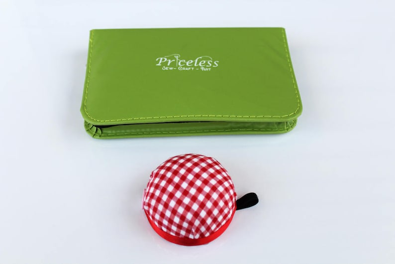 May include: A green sewing kit with the text "Priceless Sew-Craft-Knit" on the front. A red and white checked pincushion is in the foreground.