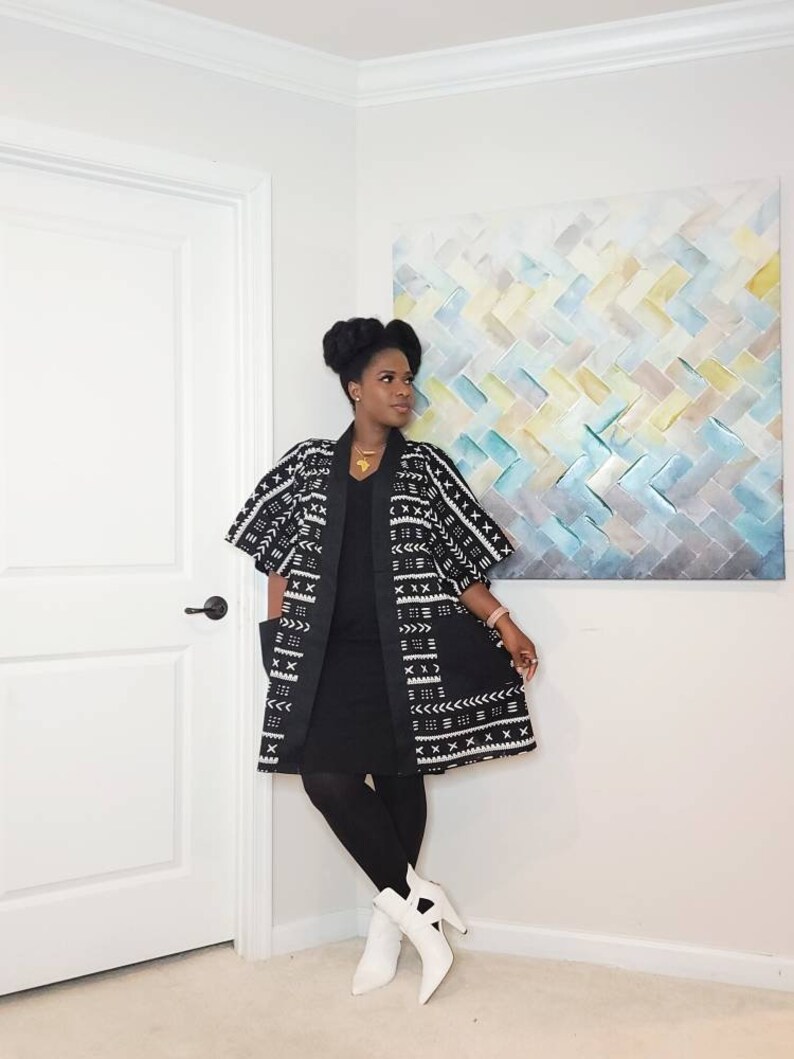 May include: A woman wearing a black dress with a white and black patterned kimono. She is wearing white ankle boots and a gold necklace.