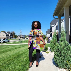 May include: A vibrant patchwork jacket, featuring a mix of patterns and colours, worn with a black belt and leggings. The jacket includes orange, yellow, blue, and purple. The outfit is completed with black heels.