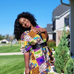 May include: A vibrant patchwork tunic with a black belt. The tunic showcases diverse patterns, such as animal print, geometric shapes, and floral motifs. It has short sleeves and is worn with black leggings.