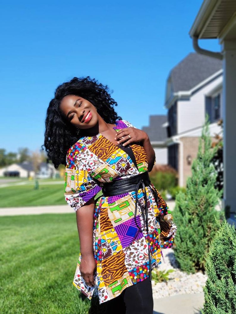 May include: A vibrant patchwork tunic with a black belt. The tunic showcases diverse patterns, such as animal print, geometric shapes, and floral motifs. It has short sleeves and is worn with black leggings.
