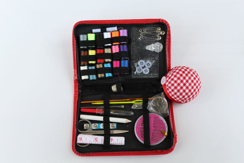 May include: A red sewing kit containing a selection of colourful threads, needles, buttons and other sewing essentials. The kit is open, revealing its contents.