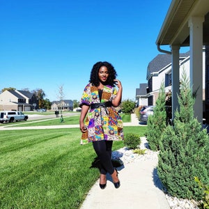 May include: A vibrant patchwork jacket, cinched with a black belt, paired with black leggings. The jacket showcases a mix of patterns and colours, including purple, yellow, and orange. Black heels complete the ensemble.