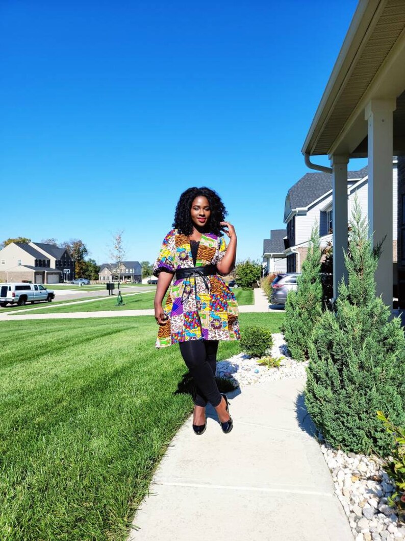 May include: A vibrant patchwork jacket, cinched with a black belt, paired with black leggings. The jacket showcases a mix of patterns and colours, including purple, yellow, and orange. Black heels complete the ensemble.