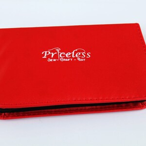 May include: Red leather case with a black zipper and the text "Priceless Sew-Craft-Art" in white.