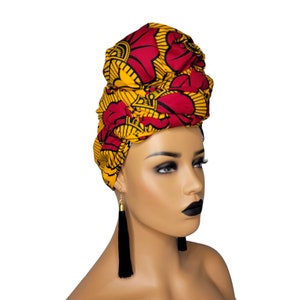 May include: A red and yellow patterned head wrap with a floral design. The wrap is tied on a mannequin's head.