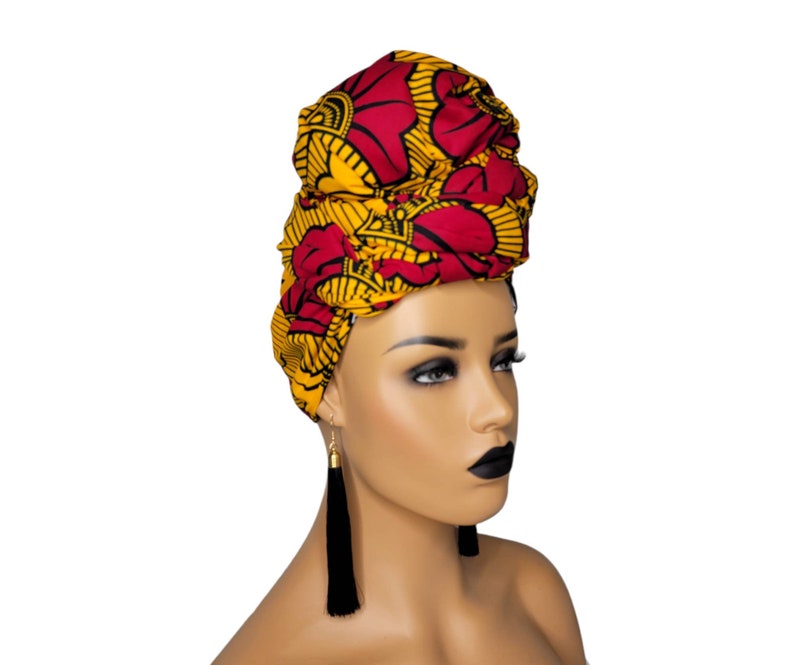 May include: A red and yellow patterned head wrap with a floral design. The wrap is tied on a mannequin's head.