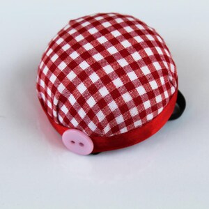 May include: Red and white gingham pincushion with a pink button and a red ribbon.