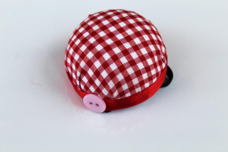 May include: Red and white gingham pincushion with a pink button and a red ribbon.