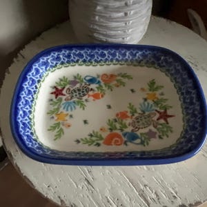May include: Rectangular ceramic serving dish with a blue rim and a white interior. The dish is decorated with sea life including turtles, starfish, and fish. The border has a blue floral design.