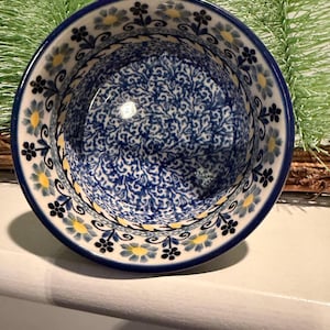 May include: A ceramic bowl with a blue floral pattern. The bowl has a dark blue rim and a white base. The interior features a detailed blue and white floral design. Yellow and black floral accents decorate the rim.