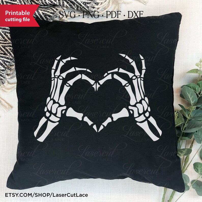 May include: A black cushion with a white skeleton hand design making a heart shape. The cushion is on a white surface with a green plant in the background. The text "Etsy.com/shop/LaserCutLace" is at the bottom of the image.