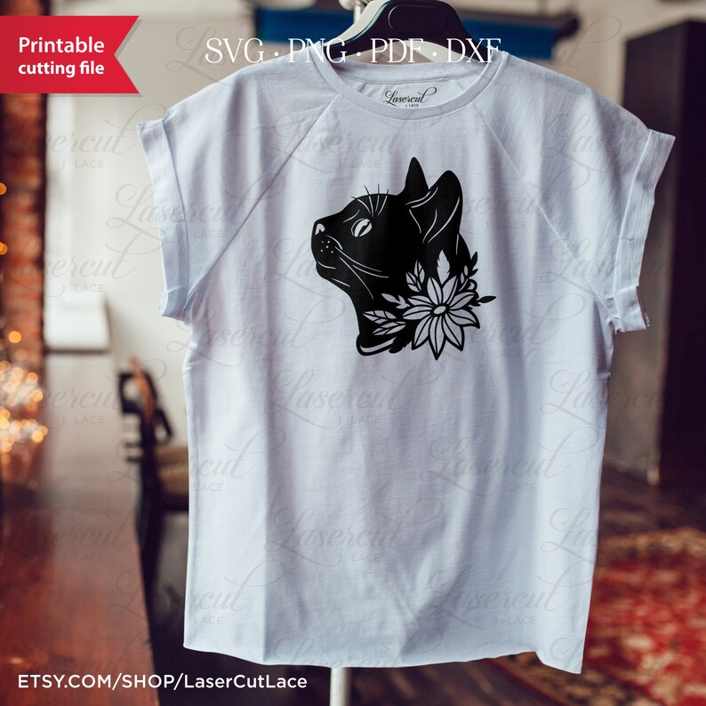 May include: A white t-shirt with a black silhouette of a cat's head with flowers around its neck. The text "Lasercut Lace" is printed on the bottom of the shirt.