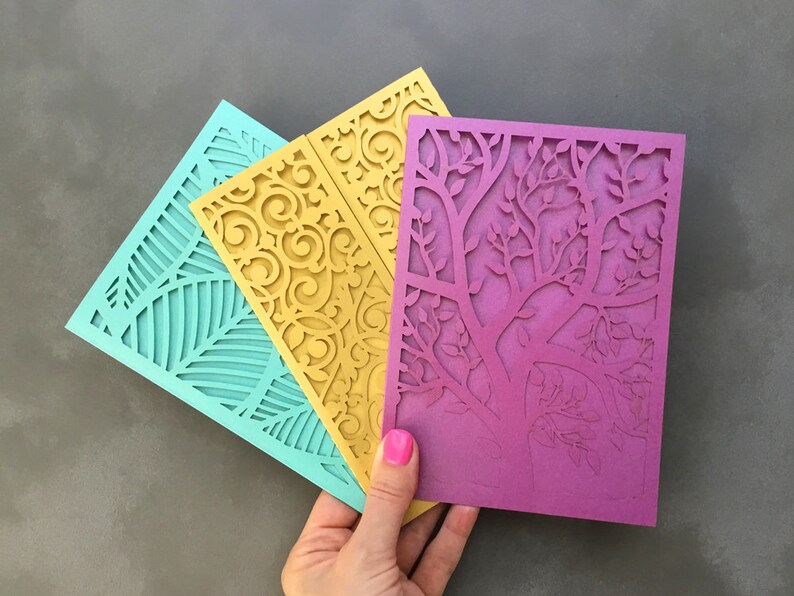 May include: Three laser cut cards with intricate designs. The card on the left is teal blue with a leaf pattern. The middle card is yellow with a floral pattern. The card on the right is purple with a tree branch pattern.