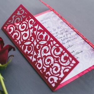 May include: A red laser-cut invitation with a delicate floral design. The invitation is folded in half and has a white interior with black calligraphy.