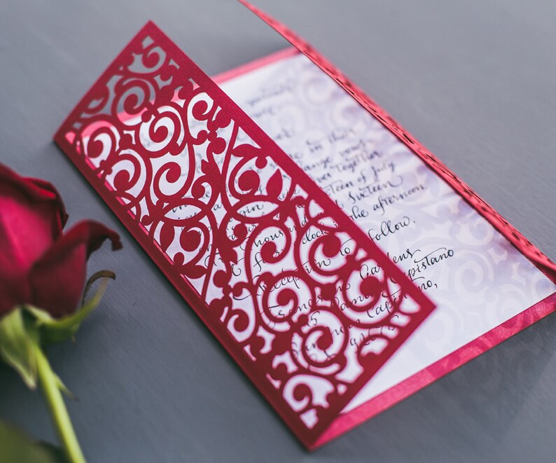May include: A red laser-cut invitation with a delicate floral design. The invitation is folded in half and has a white interior with black calligraphy.