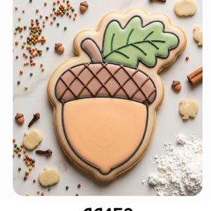 May include: A large acorn-shaped sugar cookie decorated with tan icing for the nut, brown icing for the cap with a cross-hatched pattern, and light green icing for the leaf. The text CC453 is printed below the cookie, surrounded by sprinkles.