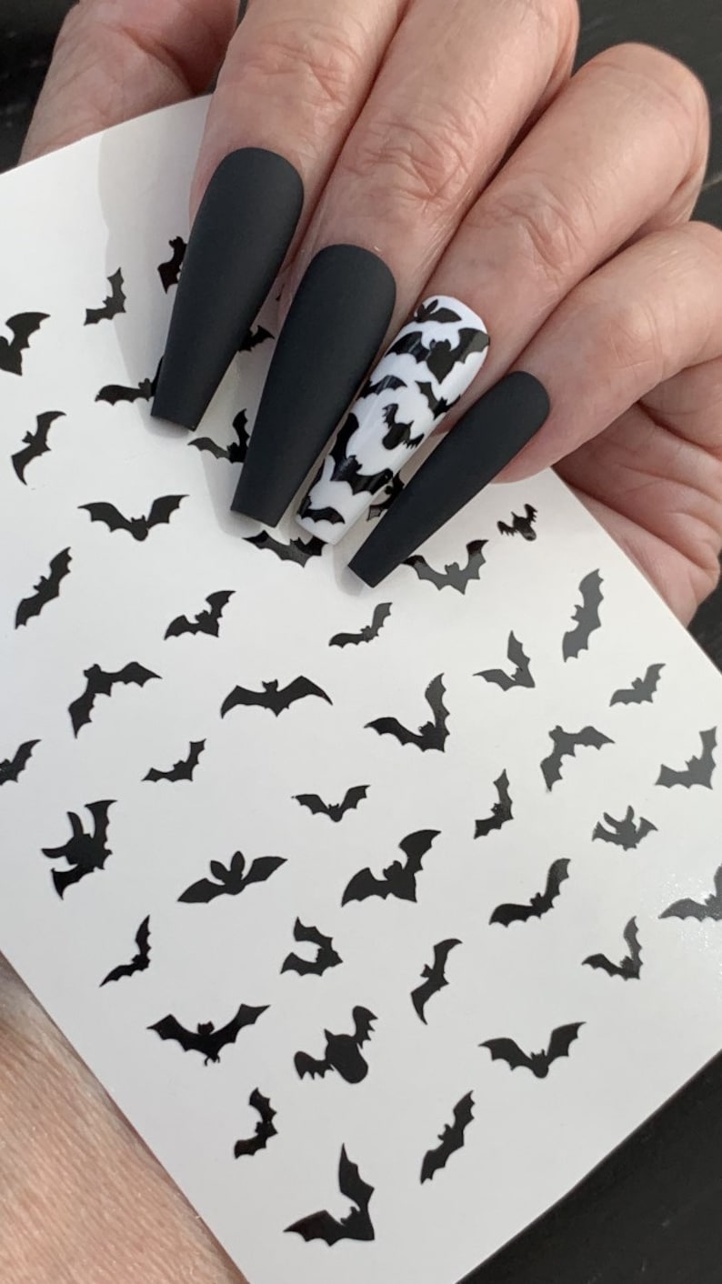 May include: A sheet of black bat nail decals on a white background. The decals are in various sizes and are perfect for adding a spooky touch to your nails.
