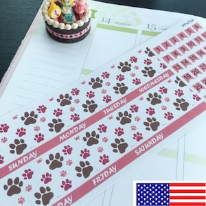 May include: A sheet of planner stickers with paw prints in brown and pink on a white background. The stickers are labeled with the days of the week: Sunday, Monday, Tuesday, Wednesday, Thursday, Friday, and Saturday.