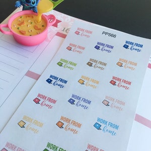 May include: A pink bowl with a cartoon character pouring soup from a green spoon. A sheet of stickers with the text "WORK FROM home" and laptop graphics in various colors is on a planner page.
