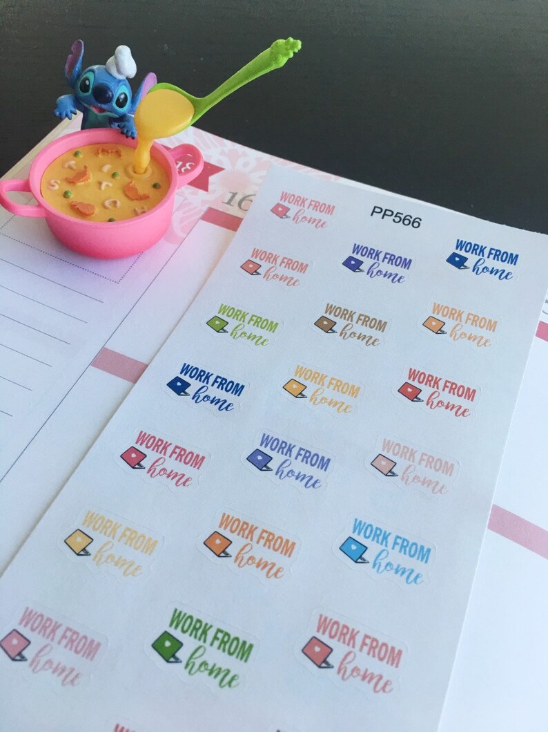 May include: A pink bowl with a cartoon character pouring soup from a green spoon. A sheet of stickers with the text "WORK FROM home" and laptop graphics in various colors is on a planner page.