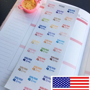 May include: A planner is open to a double-page spread with stickers that say "WORK FROM home" in various colors. A small figurine of a blue character with a spoon is near a pink bowl. The American flag is in the bottom right.