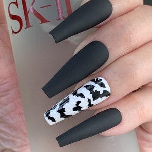 May include: Black matte long press-on nails with a white and black bat design on one nail.
