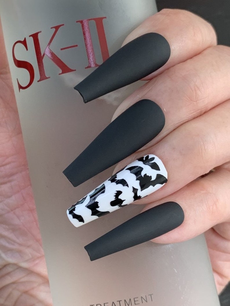 May include: Black matte long press-on nails with a white and black bat design on one nail.