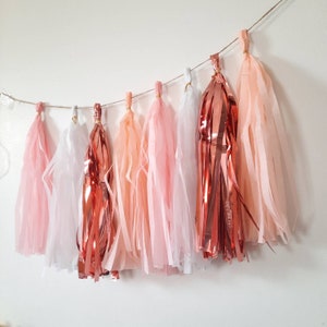 Puede incluir: Una guirnalda de borlas de papel de seda en tonos rosa, melocot&oacute;n y oro rosa. Las borlas est&aacute;n atadas con un cordel y son perfectas para a&ntilde;adir un toque de fantas&iacute;a a cualquier fiesta o evento.