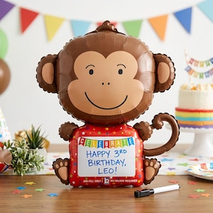 May include: A brown monkey-shaped balloon with a smiling face and a red body. The balloon has the words "CELEBRATE HAPPY 3RD BIRTHDAY, LEO!" written on it. The balloon is for air-fill only and does not require helium.