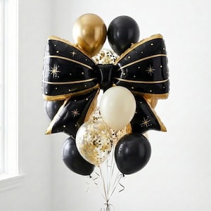 May include: A festive balloon bouquet featuring a large black bow-shaped balloon with gold trim and star accents. The arrangement includes gold, black, and confetti-filled balloons, perfect for celebrations and events.