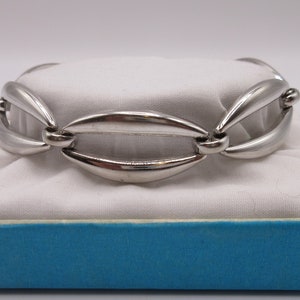 May include: A silver bracelet featuring a distinctive interlocking design. The bracelet is crafted from smooth, rounded metal links, giving it a contemporary and stylish appearance.