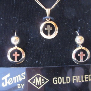 May include: Gold filled cross necklace and earrings set. The necklace and earrings feature a gold cross inside a circle. The jewelry is displayed on a black velvet background with the text "Jems by JMS GOLD FILLED".