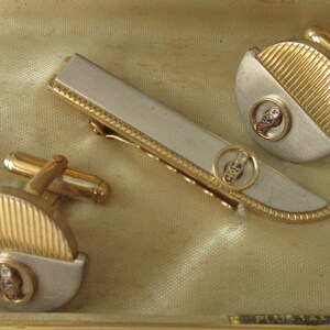 May include: A set of gold and silver cufflinks and a tie clip. Each piece features a circular design with a red, white, and blue emblem in the center.